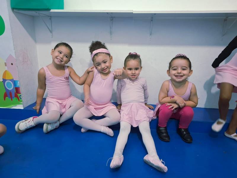 Alunas da Creche Escola Santa Beatriz sentadas durante a aula de ballet, de uniforme rosa e sapatilha