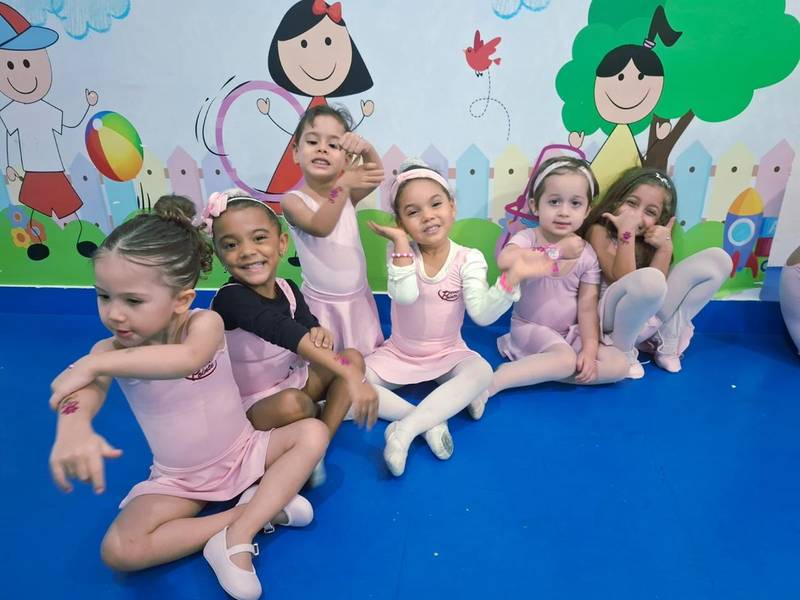 Turma de ballet da Creche Escola Santa Beatriz posando em grupo no fim da aula, em frente ao painel colorido