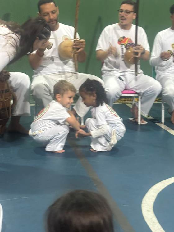 Crianças da Creche Escola Santa Beatriz na roda de capoeira, com os músicos ao fundo tocando berimbau e atabaque