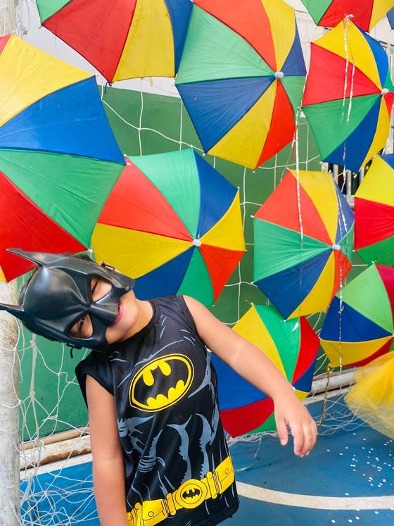 Aluno fantasiado de super-herói no Carnaval da Creche Escola Santa Beatriz, sob as sombrinhas de frevo