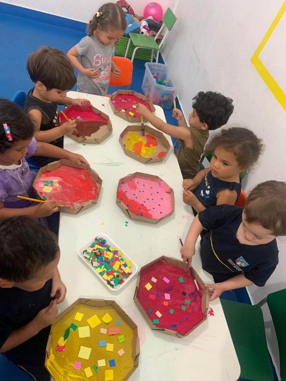 Crianças da Creche Escola Santa Beatriz pintando pizzas de papelão no ateliê da colônia de férias