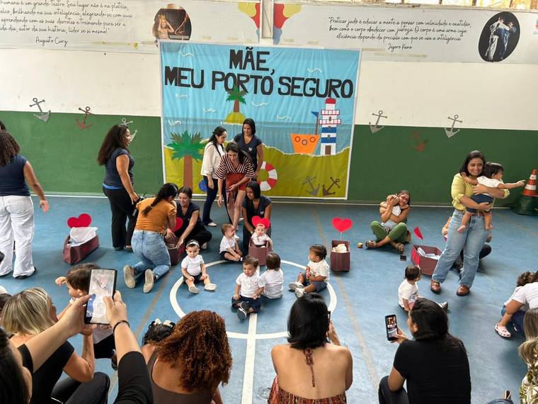 Turmas do Berçário na apresentação do Dia das Mães, na quadra da escola, em frente ao painel Mãe, meu porto seguro