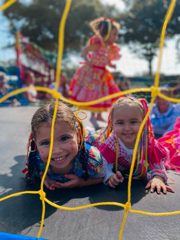 Duas alunas da Creche Escola Santa Beatriz sorrindo no pula-pula durante a Festa Junina, com trajes típicos