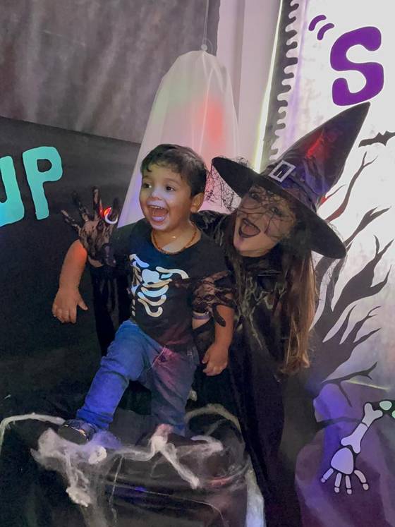 Aluno da Creche Escola Santa Beatriz rindo ao lado da bruxa na sala decorada de Halloween
