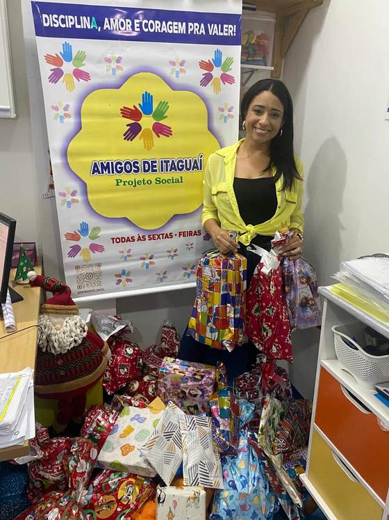 Responsável pelo projeto social parceiro com os presentes do Natal Solidário, ao lado do banner do projeto