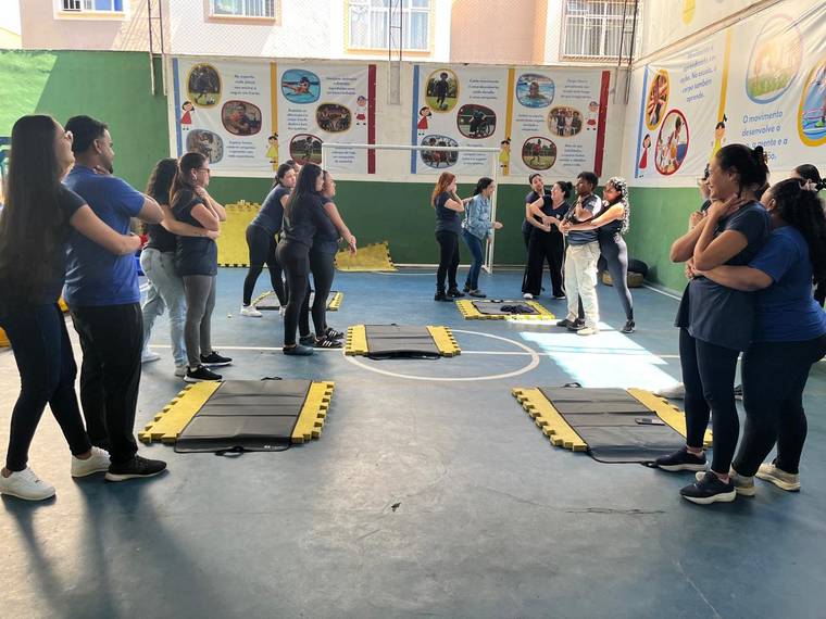 Professores e funcionários da Creche Escola Santa Beatriz praticando em duplas a manobra de desengasgo na quadra da escola